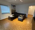 Living room with wooden floor, black sofa, coffee table, wall art, window with blinds, ceiling lights