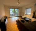 living room with wooden floor, sliding glass doors to balcony, white walls, black couch, coffee table, radiator, ceiling lights