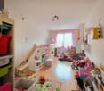 Children's room with bunk beds, slide, shelves, toys, books, and a rug