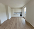 Open-concept living space with white walls, hardwood flooring, and a modern kitchen with white cabinets and a built-in dishwasher