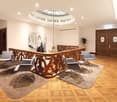 wooden handrail with a circular metal chandelier, wooden double doors, wooden flooring, two wooden chairs, round tables, carpet, white walls, artwork, and a potted plant