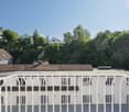 white building with brown roof, multiple windows, balcony, surrounded by trees and other houses