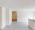 Empty room, white walls, gray floor, white kitchen counter, white cabinets, glass door, balcony