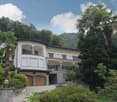 Two-story white villa with arched windows, balconies, and a tiled roof surrounded by lush greenery and palm trees