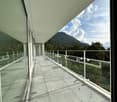 Large balcony with glass railing, overlooking a mountainous landscape with trees and cloudy sky