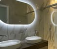 modern bathroom with double sink, shower, large mirror with lighted edges, marbled wall design