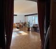 large hallway, hardwood floors, living room furniture, large window with curtains, potted plant, dining table and chairs