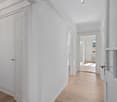 Empty hallway with white walls, wooden floor, glass doors, and a window with a view.
