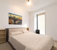 bedroom with bed, bedside table, shelf, ceiling fan, large window with balcony