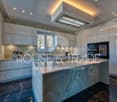 kitchen island, white marble countertop, grey tiled backsplash, built-in oven, extractor hood, cabinets, double-paned windows, glossy marble flooring