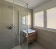 modern bathroom with shower, sink, and toilet, glass door, wooden cabinet, white tiles, large windows