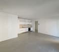 Empty room with white walls, tiled floor, kitchen area with sink, oven, and cabinets