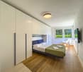 Bedroom with bed, white wardrobes, wooden floor, ceiling lamp, TV, chair, windows