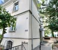 white building, 3 floors, windows with shutters, black gate, trees
