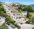 A modern apartment complex situated on the hillside with lush greenery and plants on terraces, multiple cars parked, garage, garden area
