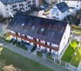 White 2-story house, brown roof, large windows, balcony on the second floor, bikes parked in front
