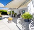 Tiled patio, shade sail, outdoor dining table, wicker chairs, plants in pots, outdoor hanging swing