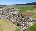 Suburban area with many detached and semi-detached houses, green fields, and a clear view of the surrounding landscape
