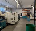Indoor facility with industrial machines, white walls, grey floor, green bucket, office equipment.