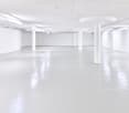 Large open-plan commercial space with white walls, concrete floors, and recessed lighting. The space appears to be empty and ready for use, with several white columns supporting the ceiling.