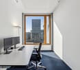 Spacious office with large window overlooking a modern city skyline, a desk with a computer setup, and a comfortable office chair.