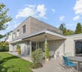 Modern architectural style, gray concrete wall, glass sliding doors, green lawn, outdoor furniture, green plants