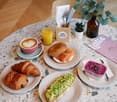 Table setting with coffee cup, bagel, avocado toast, croissants, orange juice, small plants