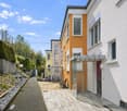 Modern apartment building, white and orange exterior, wooden walkway, bicycles parked, glass entrance, small garden area