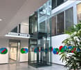 modern office building, glass elevator, white walls, colorful wall art, glass doors, plant