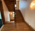 An interior hallway of a building with wooden staircases on both sides, white walls, and wooden flooring.