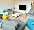 Open living space with multiple seating areas, central TV, light wooden flooring, glass window, and minimalistic decor