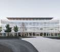 Modern office building, large glass windows, multiple floors, curved driveway, several entrance points, symmetrical design, greenery around