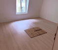 Empty room with white walls, wooden floor, window, cardboard box, and electrical outlets