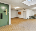 Empty storage room with wooden floor, green doors, mounted light fixtures, a cabinet, and a white door