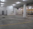 Empty warehouse with concrete floor, metal scaffolding, electrical panels, and white walls