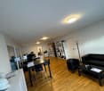 Open plan office with wooden floor, white walls, office desks, shelves, a couch, a table, and office equipment