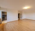 empty room with wooden floor, kitchen, two doors, and an open window to the balcony