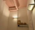 Raised ground floor, walls painted pink, white ceiling, shelves with boxes, door, pipe in the ceiling