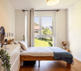 bed, pillows, curtains, cabinet, table with flowers, potted plants, large window with view