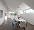 Dining room with white walls, wooden floor, large windows, white dining table, white chairs, pendant light, flower vase, couch, and paintings