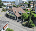 House with brown roof, solar panels, garage, balcony, multiple cars parked, green lawn, trees, street, buildings, and a view of the city