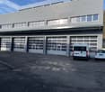 Industrial building with large garage doors, multiple windows, and a parking area in front.