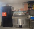 Commercial kitchen with stainless steel appliances, refrigerators, and storage shelves.