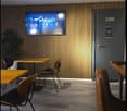 A room with wooden walls, tiled floor, a TV mounted on the wall, a potted plant, and several tables and chairs.