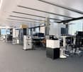 An empty office space with multiple tables, chairs, and monitors.