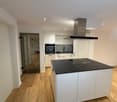 modern kitchen with white cabinets, black countertop, island with induction cooktop, built-in oven, extractor hood, wooden floor