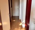 Empty hallway with wooden floor, white walls, white door, ceiling light, and a power outlet.