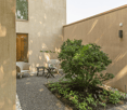 small garden with gravel, two chairs, small table, plant, beige walls