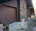 Exterior of a house with a wooden garage door, brick pathway, and potted plants.