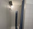 A corner of a shower with white and blue tiles, shower head, and blue shower curtain.